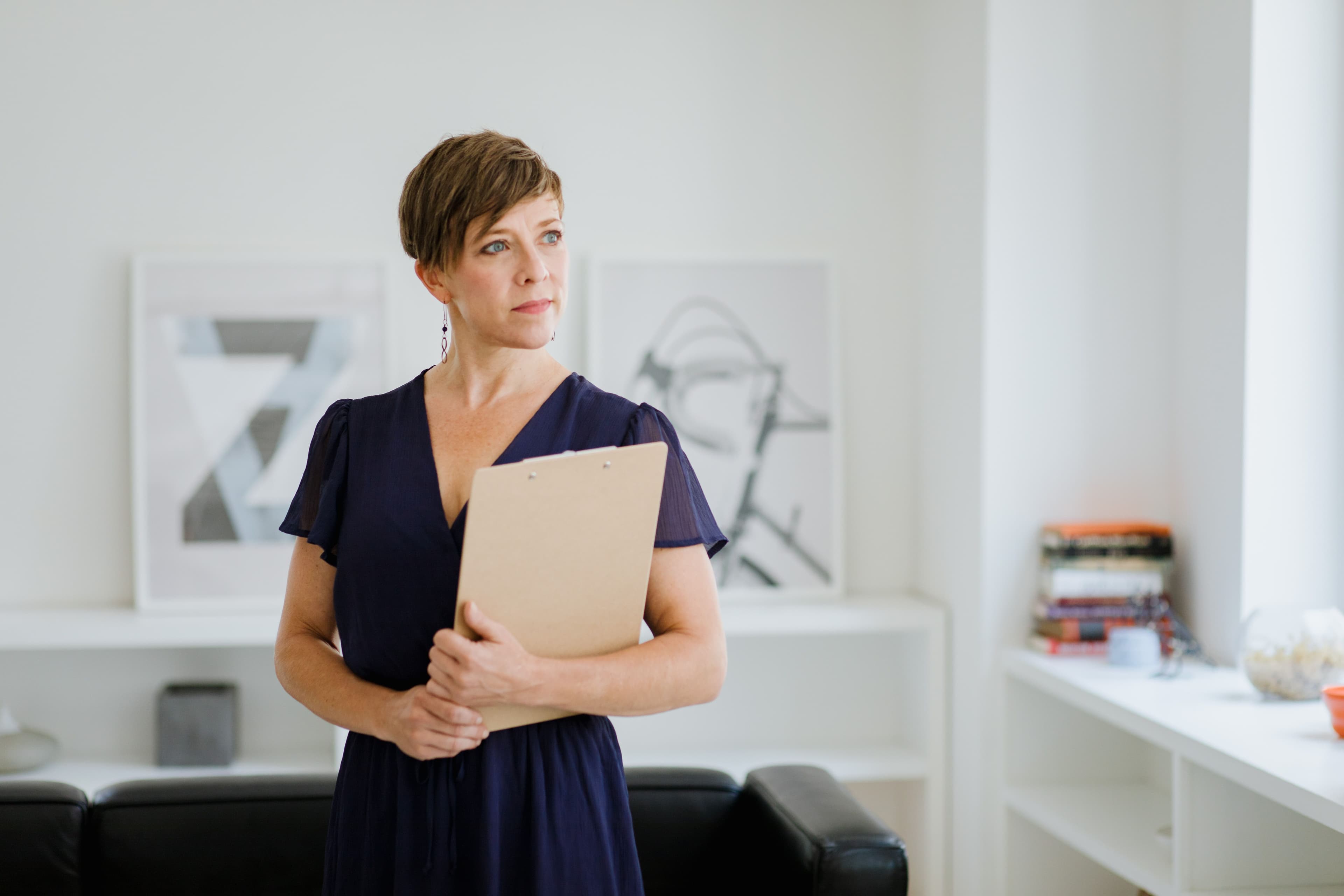 A woman holds a clipboard in a bright, minimalist living room with framed abstract art.